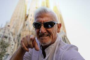hermoso medio Envejecido hombre visitando sagrada familiar, Barcelona - contento turista tomando un selfie en el calle foto
