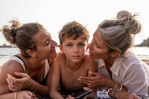 portrait of beautiful middle aged mother and her daughter kissing youngest child on the beach at sunset photo