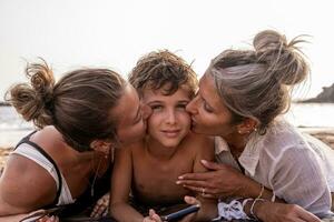 portrait of beautiful middle aged mother and her daughter kissing youngest child on the beach at sunset photo