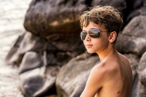 gracioso retrato de joven sin camisa hombre vistiendo Gafas de sol en un exótico playa foto