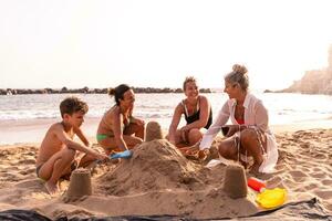 familia en vacaciones jugando con arena castillos en el playa a puesta de sol foto