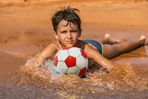 young boy playing with a soccer ball on the beach by the sea photo