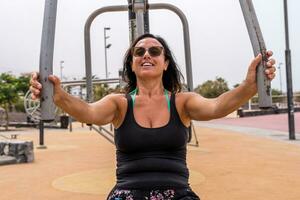 attractive middle aged woman doing gymnastic exercises in an outdoor public gym at a resort photo