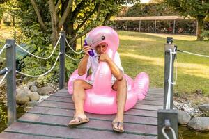 smiling handsome middle aged man having fun sitting on an inflatable flamingo toy photo