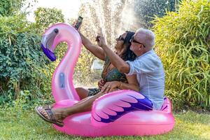 beautiful smiling middle aged couple taking a selfie sitting on flamingo inflatable toy photo
