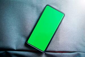 Flat lay photo of smartphone green screen. Chroma key phone screen in vertical position. Photo mockup with copy space. Internet of things. New technology concept.