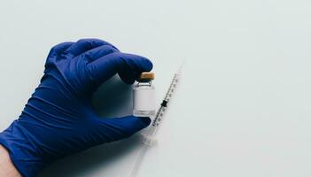 Hand with glove showing vaccine in vial with syringe over white background and copy space. Medical concept. Insurance, laboratory, subcutaneous injection. Disease treatment immunization. photo