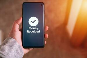 Woman transfering money online using apps on smartphone. Selective focus. Concept of financial transactions with mobile devices. Smartphone screen displaying money transfer confirmation. photo