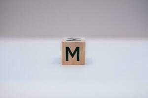 Wooden block written M with a white background, education concept, close up. photo