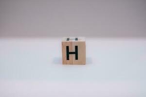 Wooden block written H with a white background, education concept, close up. photo