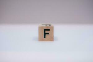 Wooden block written F with a white background, education concept, close up. photo