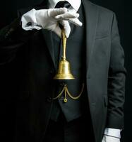 Portrait of Butler or Hotel Concierge in Dark Suit and White Gloves Holding Gold Bell. Concept of Ring for Service and Professional Hospitality. photo