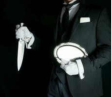 Butler in Dark Suit Holding Silver Serving Tray and a Sharp Knife. Concept of Butler Did It Classic Murder Mystery photo