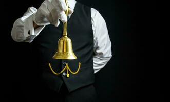 Portrait of Butler or Hotel Concierge Wearing Vest and White Gloves Holding Gold Bell. Ring for Service. photo