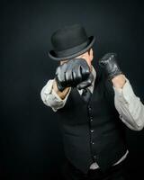 retrato de peligroso Clásico combatiente en chaleco y jugador de bolos sombrero en pie en kárate postura. gángster en negro cuero guantes. foto