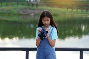 Asian girl uses binoculars to observe the nature, birds, and animals of the National Park while camping with her family. with the concept of learning outside the classroom nature study, exploration. photo