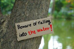 A sign posted on a tree near the pond reads, beware of falling into the water warning visitors to the pond to be careful as they might fall into the water. Soft and selective focus. photo