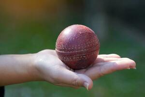 Cricket ball in Asian woman hand on green background of lawn and trees. Soft and selective focus. photo