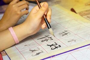 Asian students practice the art of Chinese calligraphy by writing Chinese characters, the word  ni hao , which means hello on paper. Soft and selective focus. photo