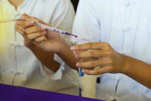 Asian students doing science experiments on chemical reactions of substances Students drop a purple solution into a test tube containing a clear solution to change it to blue. photo