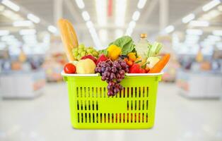 Shopping basket with fruits and vegetables in supermarket grocery store blurred background photo