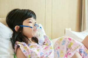Sick little asian girl inhalation with nebulizer for respiratory treatment photo