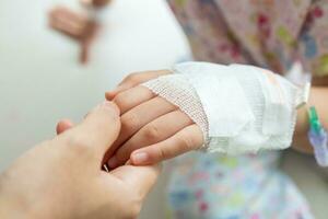 Mother holding child hand with saline IV solution in hospital photo