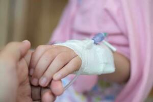 Mother holding child hand with saline IV solution in hospital photo