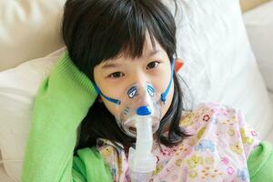 Sick little asian girl inhalation with nebulizer for respiratory treatment photo