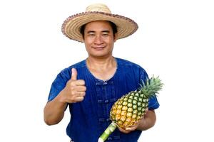 Asian man farmer wears hat, blue shirt, holds pineapple fruit, isolated on white background. Concept, Farmer is happy and proud from doing organic agriculture. Thai farmer. photo