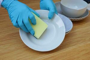 Closeup hand wear blue gloves, hold sponge to wash dish. Concept daily chore, housework. Cleaning after meals. Duty in kitchen. Wear protective gloves to protect hands from chemical substances allergy photo