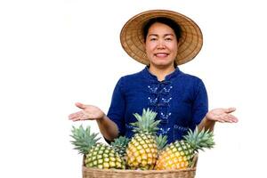 asiático mujer granjero usa sombrero, azul camisa, hacer mano gesto a presente piña frutas concepto, granjero es contento y orgulloso desde haciendo orgánico agricultura. tailandés agricultor. foto