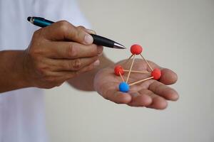 Close up teacher hands hold pen and scientific model teaching aid to teach about molecular structures, made from plasticine balls with tooth picks sticks.  Concept, science education. photo