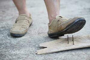 de cerca hombre vestir Zapatos es pisar en oxidado metal uña en madera. concepto, inseguro , riesgo para peligroso tétanos. ser Cuidado y Mira alrededor durante caminando en el piso o riesgo lugares. accidente foto