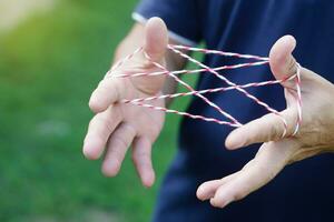 Closeup man hands is playing rope which called cats cradle game. Concept, game involving the creation of various style figures between the fingers. Traditonal playing. photo