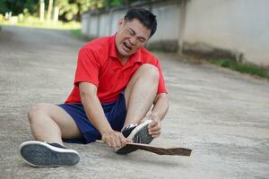 Asian man sits on floor, feels hurt after steped on nails. Concept, unsafe , risk for dangerous tetanus. Be careful and look around during walking  on the floor or risk places. Accident insurance. photo