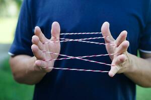 Closeup man hands is playing rope which called cats cradle game. Concept, game involving the creation of various style figures between the fingers. Traditonal playing. photo