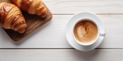 top view a cup of coffee and a croissant on a wooden table photo