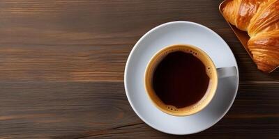 top view a cup of coffee and a croissant on a wooden table photo