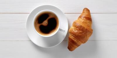 top view a cup of coffee and a croissant on a wooden table photo