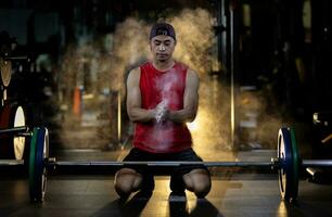 Asian muscular sport man is practice weight training on deadlift barbell for core muscle inside gym with dark background and light smoke glow for exercising and workout concept photo