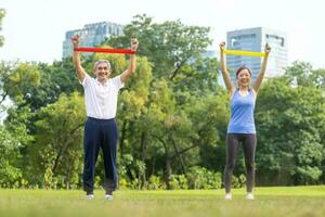 Senior asian man and his daughter are using sport rubber band to build up his arm muscle strength  in the public park for elder longevity exercise and outdoor workout photo
