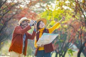 Happy Asian daughter and her senior father are walking together in public park during autumn with maple and ginkgo tree while looking at the map for fall color travel destination and family happiness photo