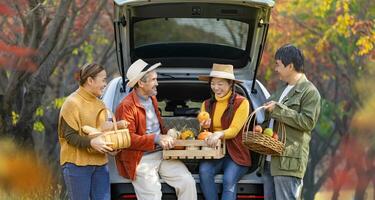 Happy Asian farmer family with senior parent are carrying produce harvest with homegrown organics apple, squash and pumpkin with fall color from maple tree during autumn season for agriculture photo