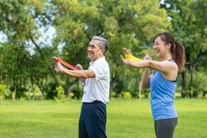 Senior asian man and his daughter are using sport rubber band to build up his arm muscle strength  in the public park for elder longevity exercise and outdoor workout photo