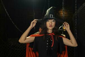 Asian girl in witch costume giving kiss for halloween party trick or treat with dark black background concept photo