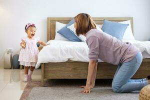 Mother is playing peek a boo or hide and seek with her little baby toddler in the bedroom while the girl is laughing in happiness for good parenting and healthy raising kid concept photo