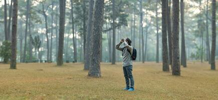 Bird watcher is looking through binoculars while exploring in the pine forest for surveying and discovering the rare biological diversity and ecologist on the field study photo