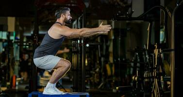 Caucasian man with strong and muscular firm shape is training on leg day by doing advance jump squat for thigh and calf muscle in gym for healthy and strong lower body weight strength with copy space photo