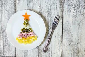 Christmas tree from a salad olivier in plate on a white wooden table. Top view with a copy space photo